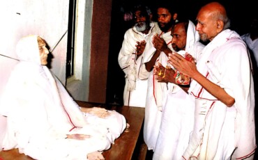 Several men dressed in white robes are gathered around Pujya Bapu, creating a scene of reverence and contemplation.