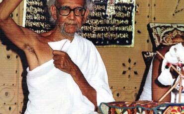 Jambuvijayji Maharaj Saheb, sits contemplatively at a table, exuding tranquility and wisdom.